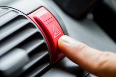 a person pressing the button on an air vent in a car or truck that is red and black