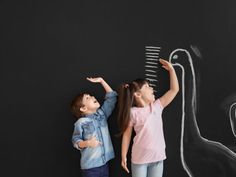 two children standing in front of a blackboard with a drawing of a bird on it