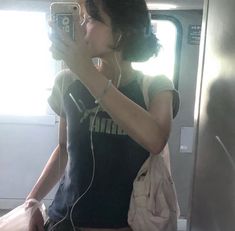 a woman with headphones is taking a selfie in the mirror on a train