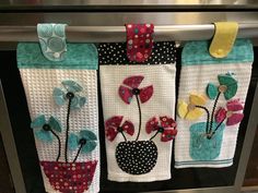 three kitchen towels hanging on the oven door with flowers in vases and polka dots