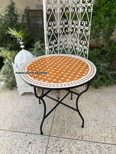 an outdoor table with white and brown dots on it, sitting in front of a wrought iron fence