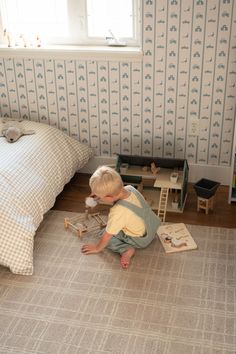 a little boy playing with toys on the floor in a bedroom next to a bed