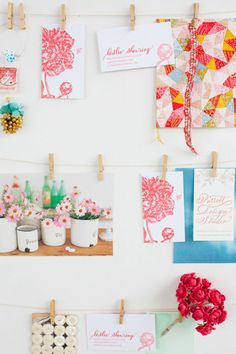 there are many cards hanging on the wall with clothes pins and flowers in vases