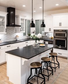 a kitchen with white cabinets, black counter tops and an island in front of the stove