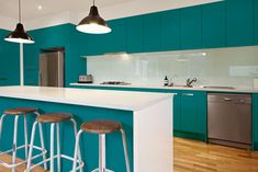 a kitchen with teal walls and white counter tops, wooden flooring and bar stools