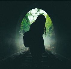 a woman with a backpack is standing in a dark tunnel looking at the light coming through