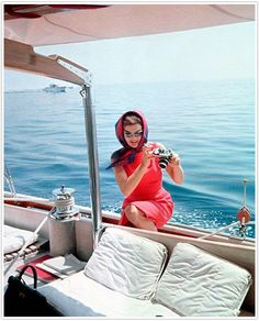 a woman sitting on the back of a boat in the water with pillows and blankets