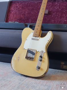 an old yellow guitar sitting in front of a case