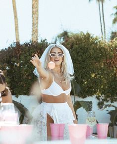 a woman in a white dress blowing bubbles at a table with pink cups on it