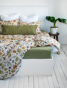 a bed with green and white sheets, pillows and blankets on top of it next to a potted plant