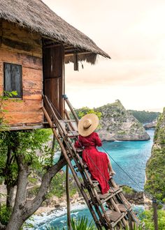 a woman in a red dress and straw hat is sitting on a ladder