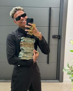 a man in sunglasses and black shirt taking a selfie with his cell phone while holding stacks of money