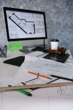 a desktop computer sitting on top of a desk covered in construction drawings and pencils