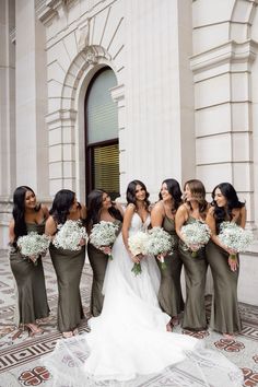 a group of women standing next to each other in front of a building holding bouquets