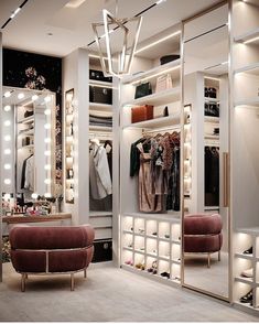 a walk in closet filled with lots of clothes and lights hanging from the ceiling next to a couch