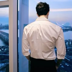 a man standing in front of a window looking out at the water and bridge below