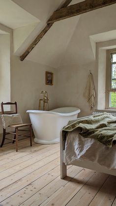 a bedroom with a bed, chair and bathtub in it next to a window