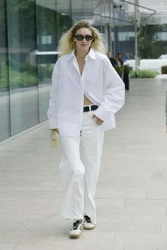 a woman with blonde hair walking down a sidewalk wearing white pants and a white shirt