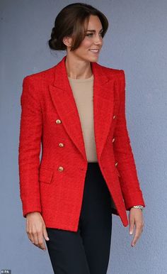 a woman in a red jacket and black pants smiles as she stands against a wall