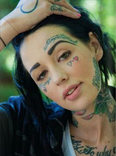 a woman with tattoos on her face posing for the camera and holding her hand up to her head