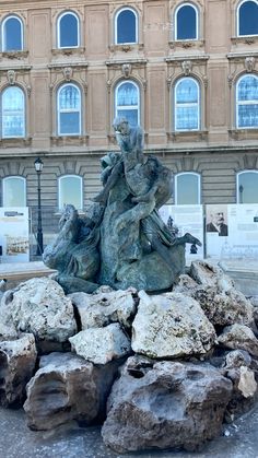 there is a statue in the middle of some rocks and snow on the ground next to a building