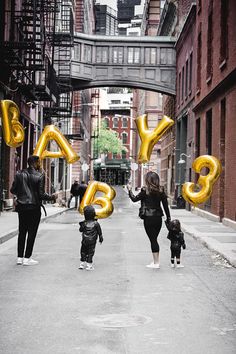 a family walking down the street with balloons in the shape of letters that spell out baby