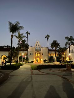 a large white building with palm trees in front of it at night time and lights on