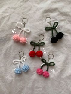 four crocheted cherries with bows and hearts on them sitting on a white sheet