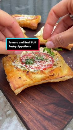 someone is picking up some food from a wooden cutting board with the words tomato and basil puff pastry appetizers