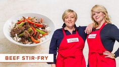 two women in red aprons standing next to a bowl of food with shrimp and clams