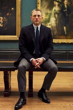 a man in a suit and tie sitting on a bench next to a large painting