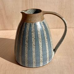 a blue and white striped pitcher sitting on top of a wooden table next to a wall