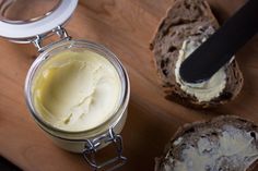 a jar of cream sitting on top of a wooden table next to some loaves of bread