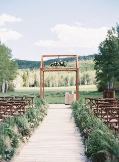 an outdoor ceremony setup with wooden chairs and greenery