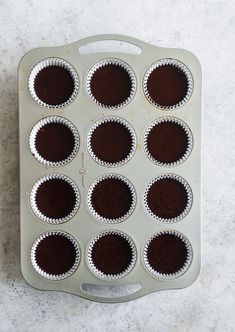 a muffin pan filled with chocolate cupcakes on a white counter top next to a knife