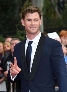 a man in a suit and tie giving the peace sign with his hand while standing on a red carpet