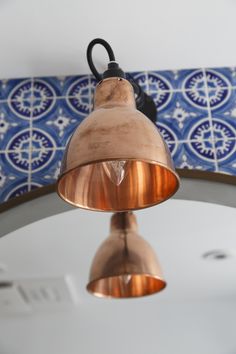 a copper colored light hanging from the ceiling in a room with blue and white tiles