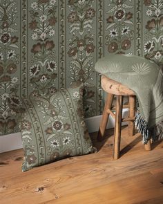 two pillows sitting on top of a wooden stool next to a wall with floral designs