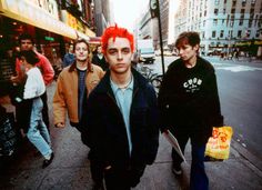 the young men are walking down the city street with their bags in hand and one has red hair