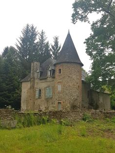 an old stone house in the middle of a field with trees around it and grass on the ground