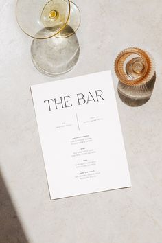 the bar menu is next to two wine glasses and an empty glass on a table