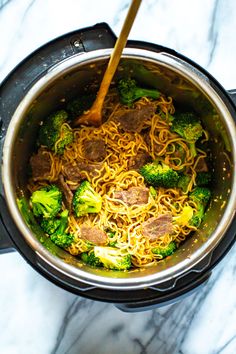 a pot filled with noodles and broccoli on top of a marble counter