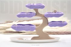 there is a purple tree with jewelry on it in front of a white plate and some feathers