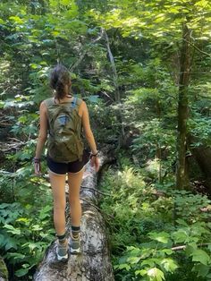 a woman walking across a log in the woods