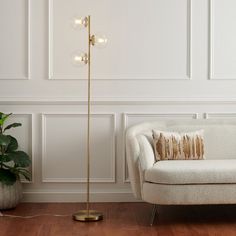 a living room with a white couch and a gold floor lamp in the corner next to a potted plant