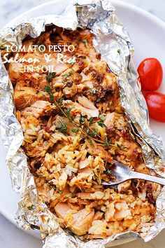 a white plate topped with chicken and rice covered in tin foil next to two tomatoes