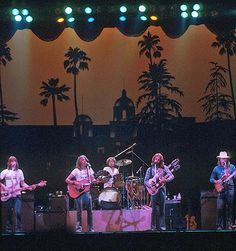 a group of people that are on stage with guitars in front of some palm trees