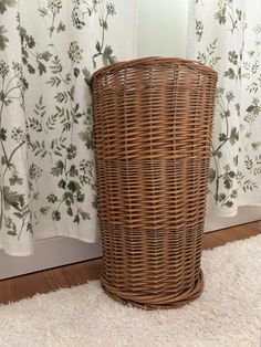 a wicker basket sitting on the floor next to a window with curtains behind it