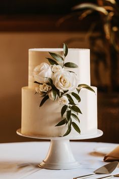 a wedding cake with white flowers and greenery on the top is ready to be cut