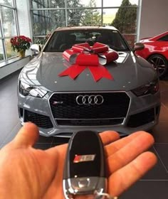 a hand holding a car key in front of a gray audi with a red bow on it